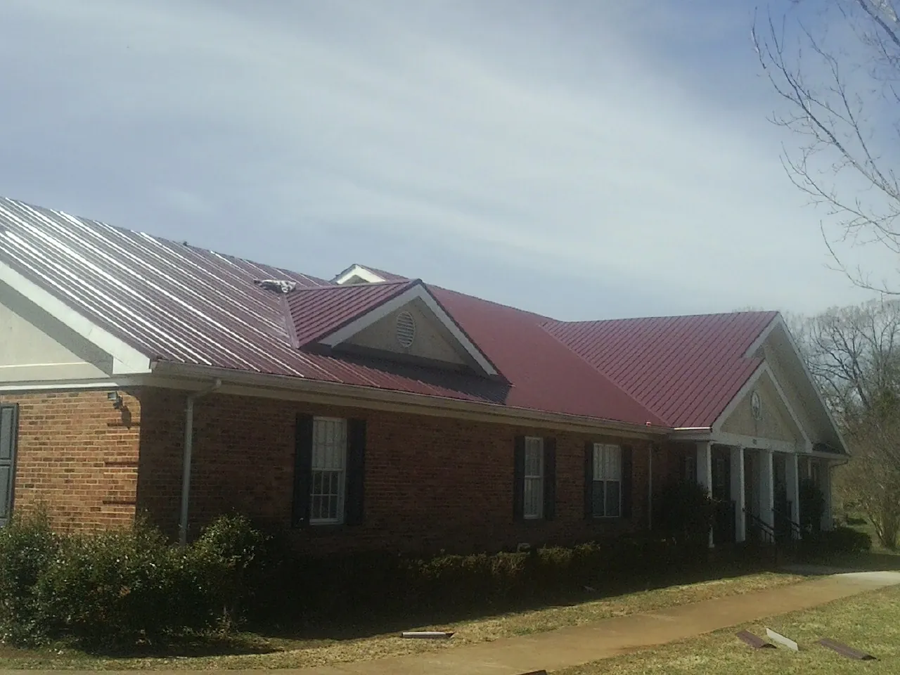 Red metal roof with gabled entries on a long brick building, from a Hail Damage Roof Repair job in Charleroi