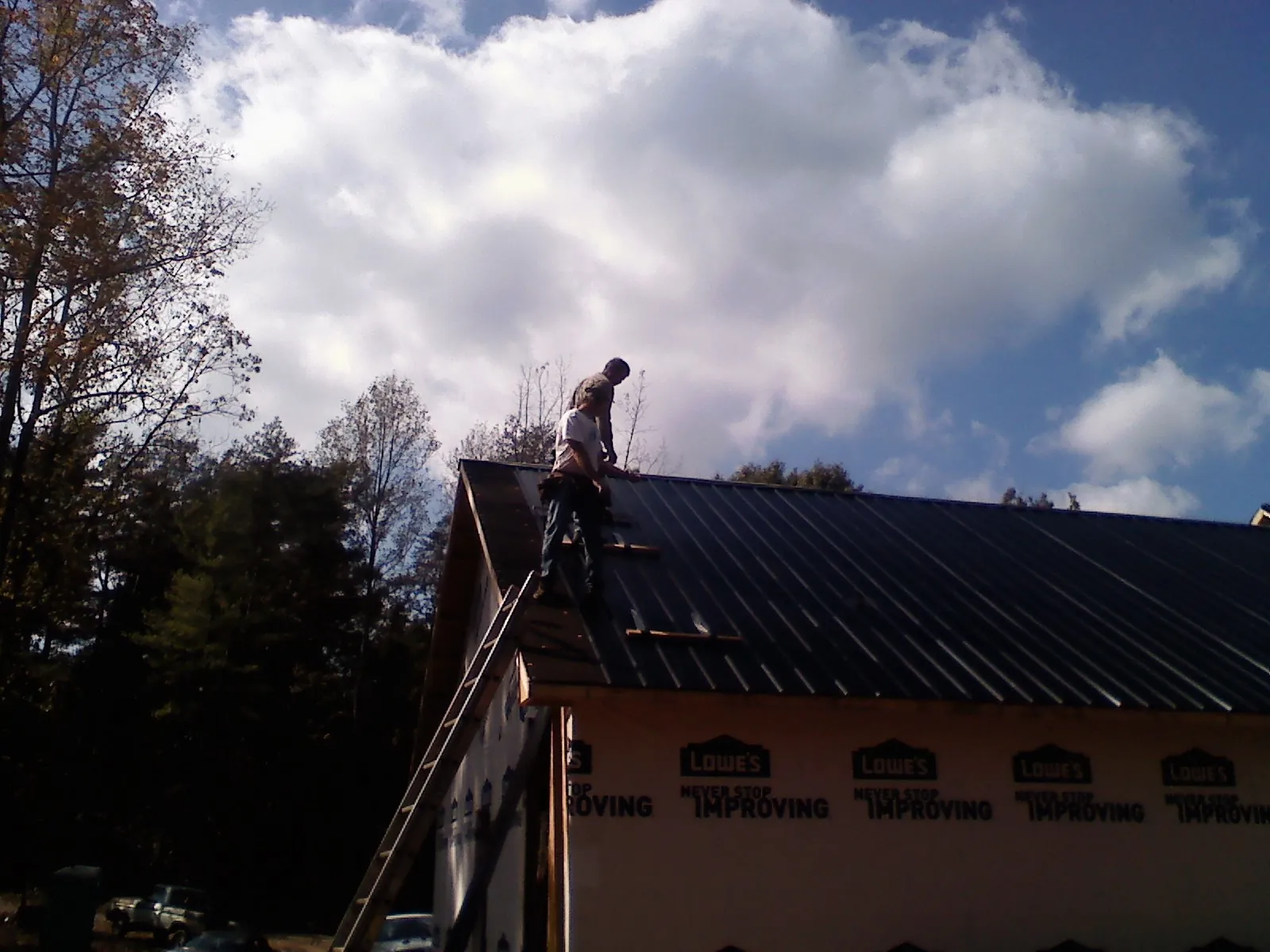 Roofer fastening dark metal panels high against a cloudy sky, from a Roof Inspection job in Charleroi