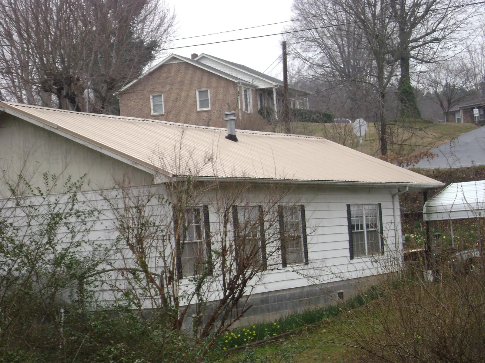 Tan metal roof on a white sided house set into a hillside — Commercial Roofing by Roofing Brothers in Charleroi